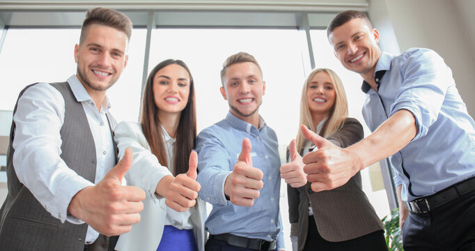 Portrait of happy businesspeople standing in office showing thumb up
