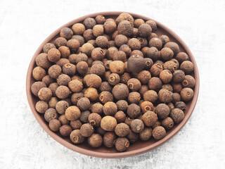 Spice Allspice (Jamaica pepper, Pimento) in clay plate on white concrete background. Macro. Healthy eating concept