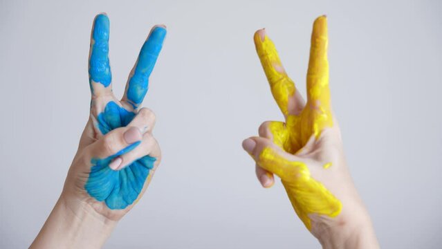 Closeup view 4k video footage of two female hands painted in blue and yellow colors of ukrainian national flag. Happy adult woman showing V letter or victory sign or symbol gesture with two fingers