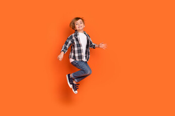 Full size profile side photo of young cheerful boy have fun jump up isolated over orange color background - obrazy, fototapety, plakaty