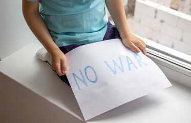 a little boy is holding a piece of paper on which is written no to war