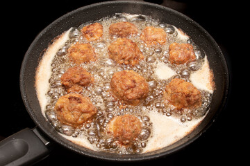 Meatballs frying in a pan, bubbles from the hot oil. Isolated on black background.