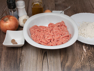 The ingredients to make meatballs, top view. On a wooden counter. Minced meat, onion, garlic, parsley, oil, flour, salt, ground black pepper, egg, nutmeg.