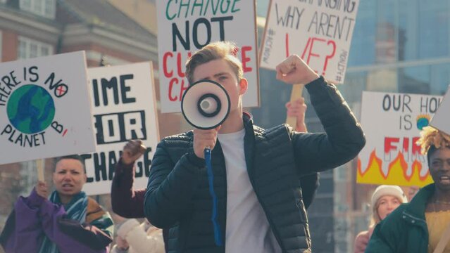 Group of protestors using megaphone holding placards and chanting slogans on demonstration march to promote awareness of climate change - shot in slow motion
