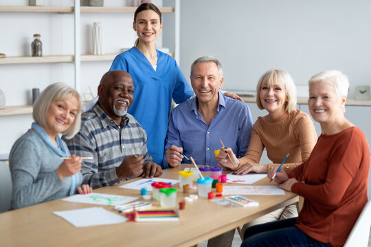 Cheerful nurse posing with senior people while having art-therapy class