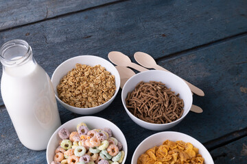 High angle view of milk bottle with various breakfast cereals in bowls by spoons on table