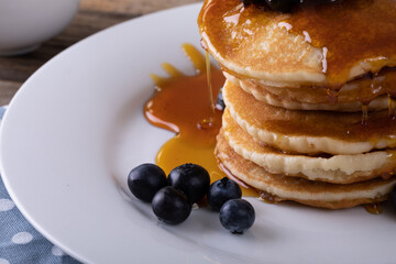 Close-up of stacked pancake served with dripping syrup and fresh blue berries in plate