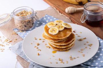 High angle view of banana slices over pancakes served in plate on napkin by oatmeal and honey jar