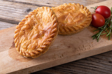 Close-up of stuffed pies with tomatoes and rosemary served on wooden serving board at table