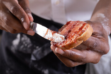 Midsection of african american male baker applying jam on bread slice