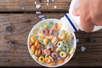 Close up view of hand pouring a milk in a bowl of cereal with copy space on wooden surface