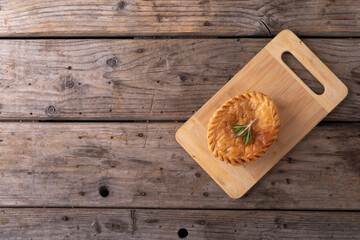 Overhead view of baked stuffed pie with rosemary on wooden serving board at table