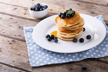 Blue berries with syrup and herb on stacked pancakes in plate over napkin at table