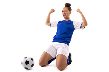 Cheerful biracial young female player with clenched fist shouting while kneeling by soccer ball