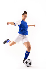 Full length of biracial young female player with arms outstretched kicking ball while playing soccer
