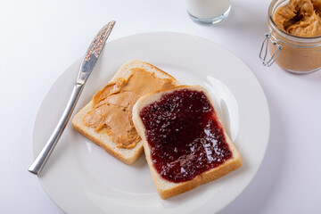 Close-up of peanut butter and preserves on bread slices in plate with table knife, jar and milk