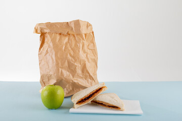 Green apple with peanut butter and jelly sandwich by paper bag at table against gray background