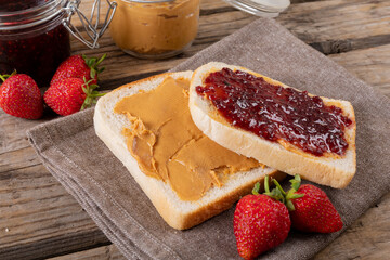 Close-up open face peanut butter and jelly sandwich on napkin with jars and strawberries at table