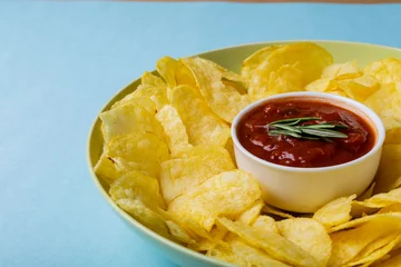  Close-up of red sauce in bowl amidst potato chips served in plate on blue background © WavebreakMediaMicro