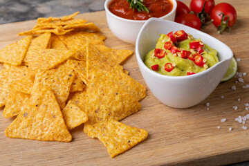 Close-up of nacho chips with dipping sauces and tomatoes served on serving board