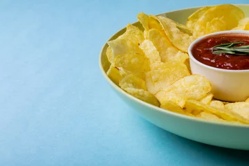  Close-up of red sauce in bowl amidst potato chips served in plate on blue background with copy space © wavebreak3