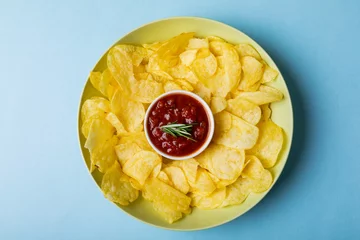  Overhead view of red sauce in bowl amidst potato chips served in plate on blue background © WavebreakMediaMicro