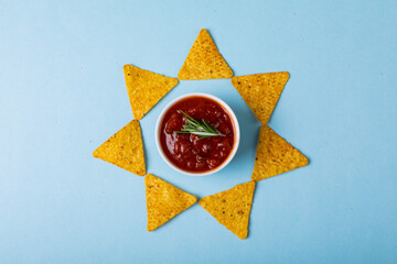 Red sauce with rosemary amidst nacho chips arranged in star shape on blue background