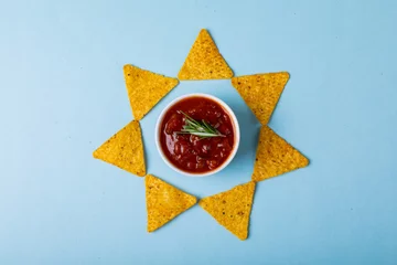 Poster Red sauce with rosemary amidst nacho chips arranged in star shape on blue background © wavebreak3