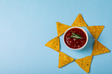 Red sauce with rosemary amidst nacho chips arranged in star shape on blue background with copy space