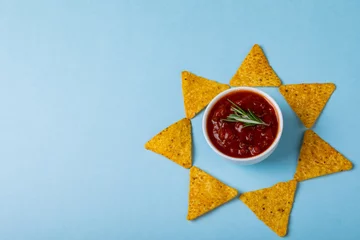 Poster Red sauce with rosemary amidst nacho chips arranged in star shape on blue background with copy space © WavebreakMediaMicro