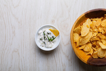 Overhead view of white dipping sauce with herbs served by potato chips in bowl on table