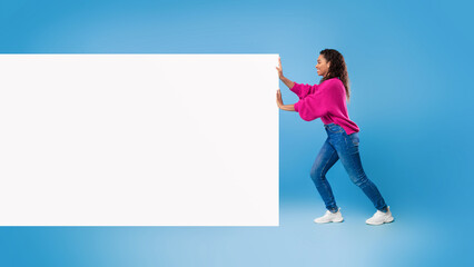 Full length of young African American lady pushing blank white paper banner with space for ad on blue background. Mockup