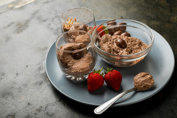 Close-up of chocolate mousse with coated nuts and strawberries served in bowl and glasses on plate