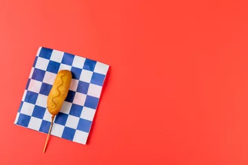  High angle view of corn dog with mustard sauce on checked pattern paper over red background © wavebreak3