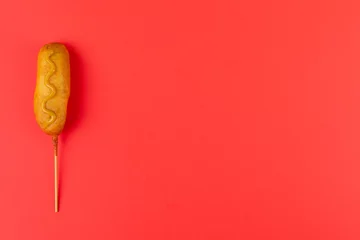  Directly above shot of corn dog with mustered sauce over skewer on red background with copy space © WavebreakMediaMicro