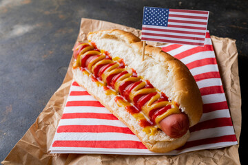 Close-up of american flag on hot dog with mustered and tomato sauce on brown wax paper at table