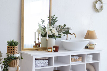 Obraz na płótnie Canvas Beautiful bathroom interior. Large mirror in a golden frame, white shell, white flowers, candles, green flowers. Organization of space in the bathroom.