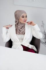 Muslim woman in hijab businesswoman sits at the table. A woman in a white jacket and headscarf. White table. Copy space. Mock up.
