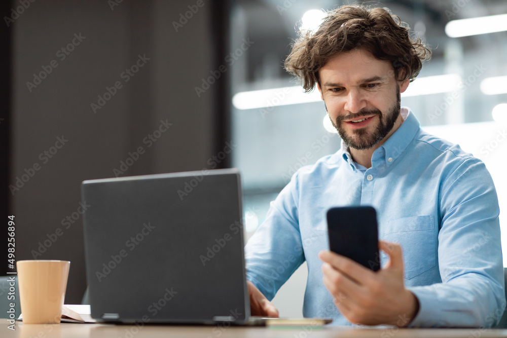 Poster portrait of smiling man using smartphone and pc at office