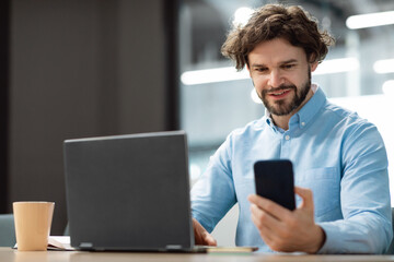 Portrait of smiling man using smartphone and pc at office