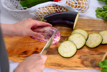 women's hands cut eggplant with knife on wooden Board, process of cooking moussaka