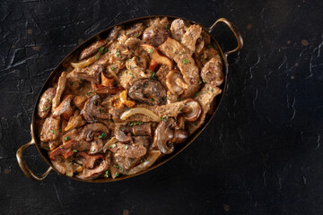 Mushroom beef stroganoff. Meat with champignons, boletus and ceps in a creamy sauce, in a skillet, shot from the top on a black background