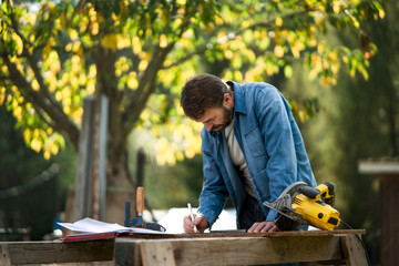 Handyman measuring a board, outside in garden.