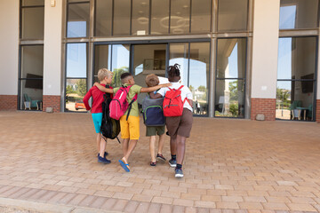 Full length rear view of elementary schoolboys with arm around and backpacks walking towards school