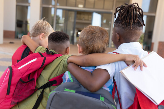 Rear view of multiracial elementary schoolboys with arm around standing at school campus