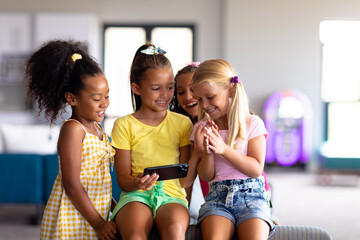 Cheerful multiracial elementary schoolgirls looking at smart phone in school