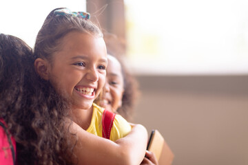 Close-up of multiracial cheerful elementary schoolgirls embracing while standing in school
