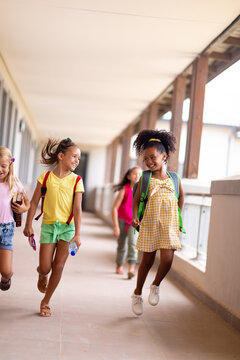 Full length of cheerful multiracial elementary schoolgirls walking in corridor