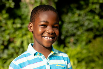 Portrait of cute happy african american boy standing against plants outdoors © wavebreak3