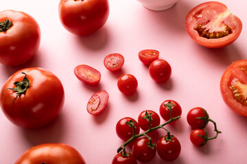 High angle view of fresh tomatoes and cherry tomatoes on pink background